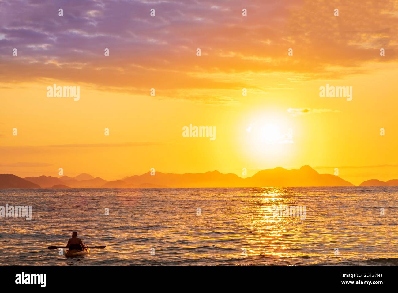 Un canoéiste à l'aube avec le soleil levant sur une baie océanique tropicale calme et des collines lointaines Banque D'Images