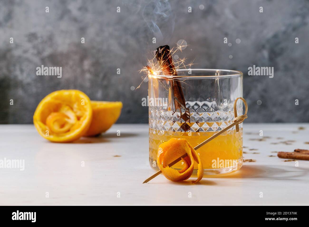 Verre de jus d'orange Whisky cocktail avec alcool tourbillonnait d'orange et bâtons de cannelle fumeurs debout sur la table en marbre blanc avec golden Banque D'Images