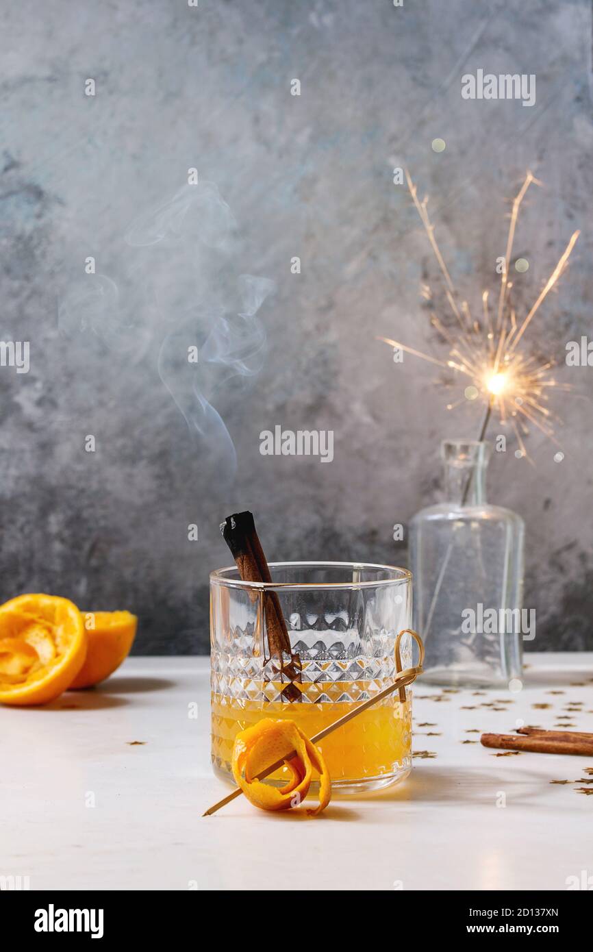 Verre de jus d'orange Whisky cocktail avec alcool tourbillonnait d'orange et bâtons de cannelle fumeurs debout sur la table en marbre blanc avec golden Banque D'Images