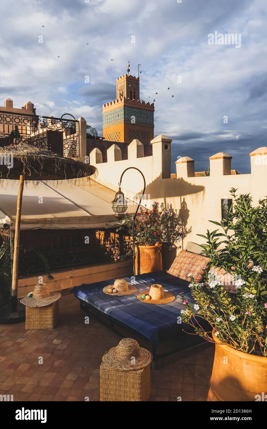 Belle terrasse d'hôtel-salon dans le centre-ville de Marrakech au coucher du soleil. Décor marocain avec éléments vintage : lanterne en métal, chapeau en osier, lit et parapluie. Banque D'Images