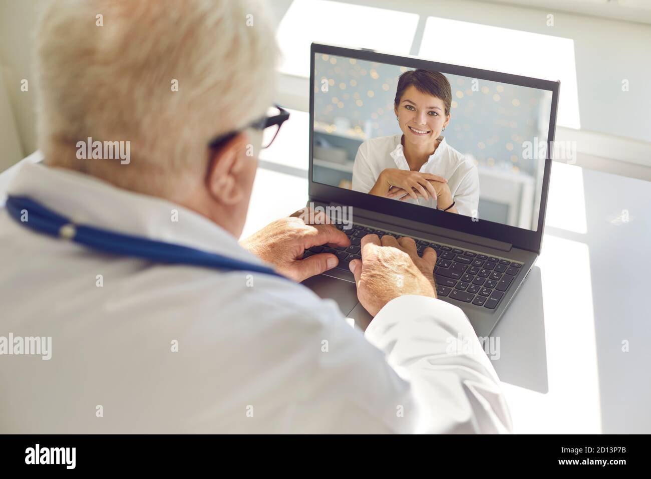 Homme mature médecin assis à un bureau dans le bureau donnant la vidéo consultation à la femme heureuse Banque D'Images