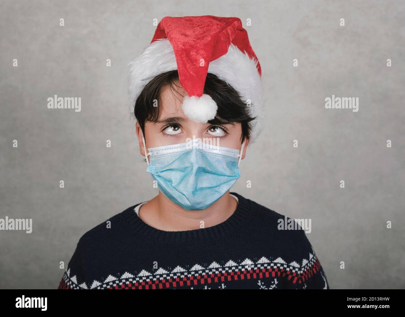 Joyeux Noël, drôle d'enfant avec masque médical portant chapeau de Père Noël sur fond gris Banque D'Images