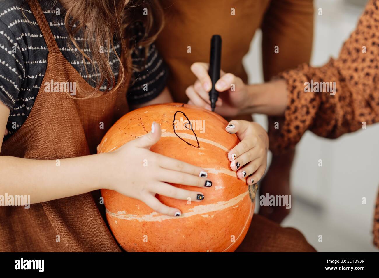 jeune fille assise à une table, décorant des citrouilles. Les vacances d'Halloween et le style de vie de famille. Petite fille peint une citrouille pour Halloween Banque D'Images