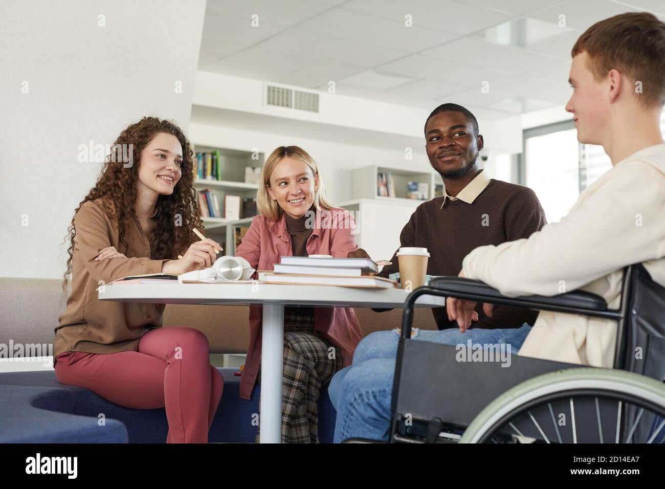 Vue en contre-plongée d'un groupe multiethnique d'étudiants qui étudient dans bibliothèque de l'université avec un jeune homme en fauteuil roulant en premier plan Banque D'Images