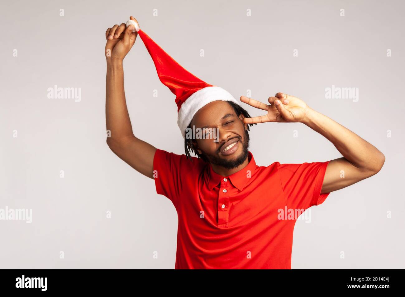 Homme afro-américain joyeux et positif avec des dreadlocks dans le chapeau rouge du père noël ayant du plaisir à montrer le geste de paix, noël et la fête du nouvel an. Indoo Banque D'Images