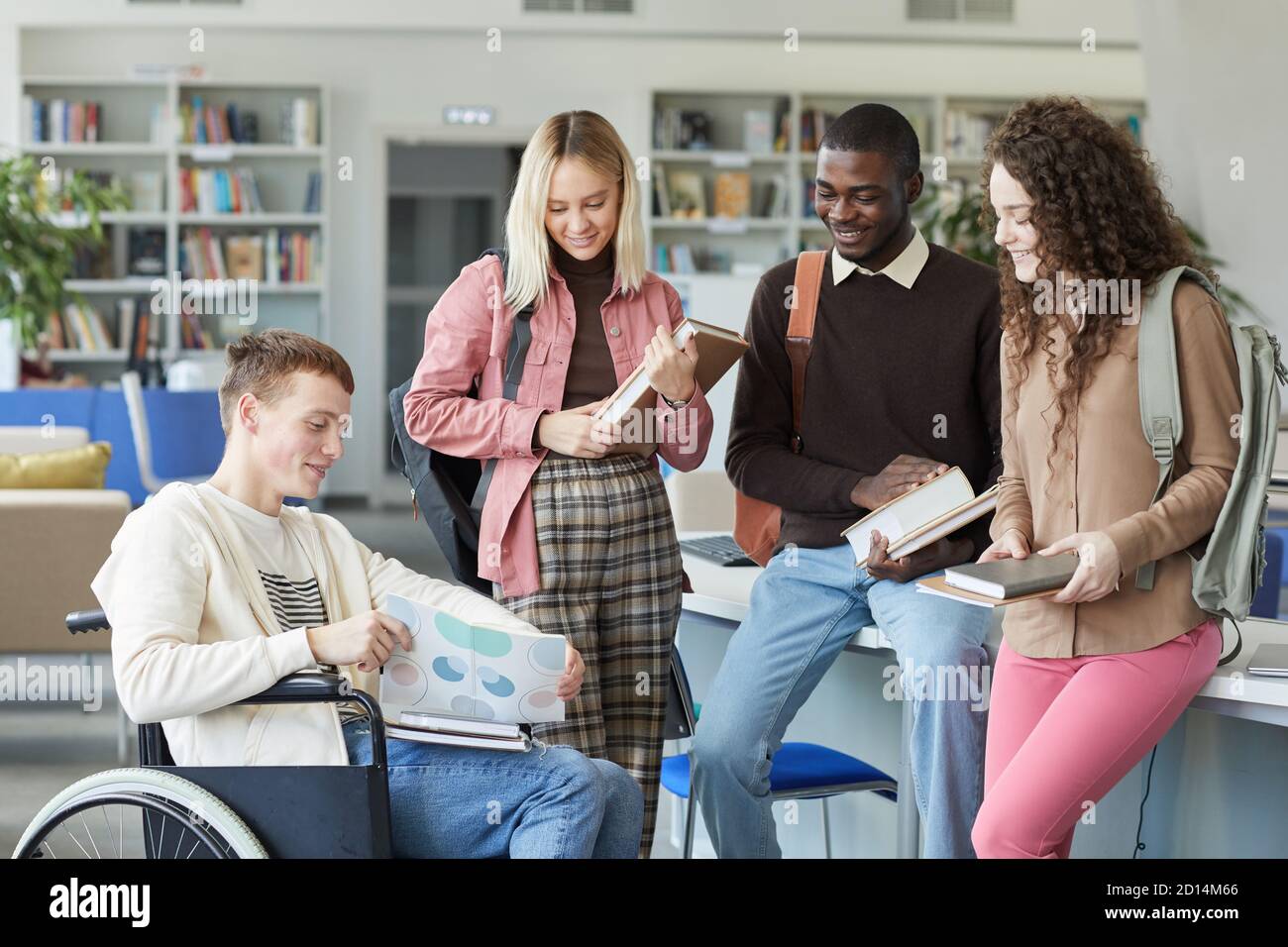 Portrait d'un groupe multiethnique d'étudiants dans la bibliothèque du collège avec garçon en fauteuil roulant en premier plan Banque D'Images