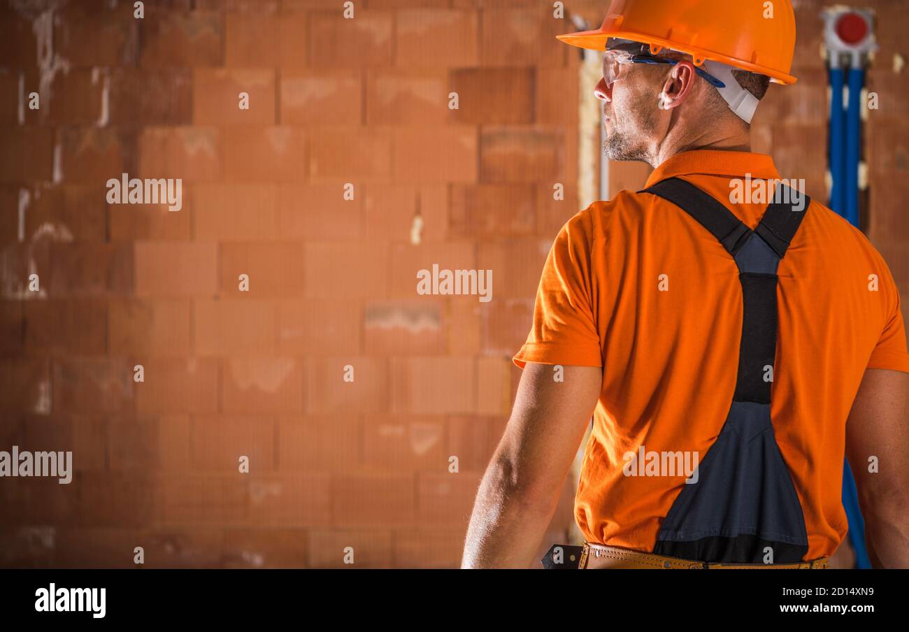 Travailleur de l'industrie de la construction caucasienne dans ses 40 ans portant un casque de sécurité orange et des lunettes de sécurité se préparant pour une autre journée complète sur le site de construction. Banque D'Images