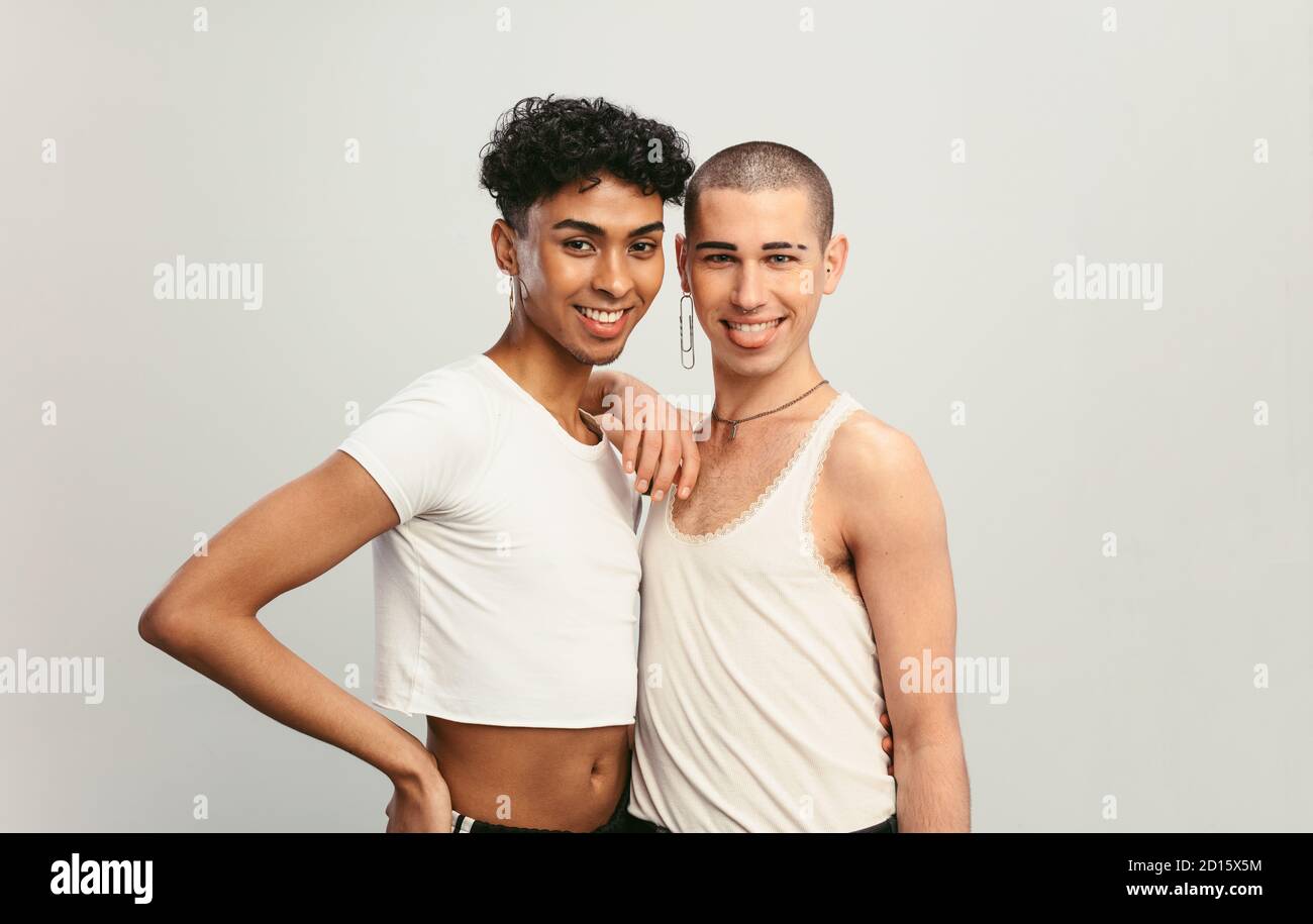 Portrait de deux beaux hommes gais debout ensemble. Deux amis masculins avec boucles d'oreilles regardant la caméra sur fond blanc. Banque D'Images