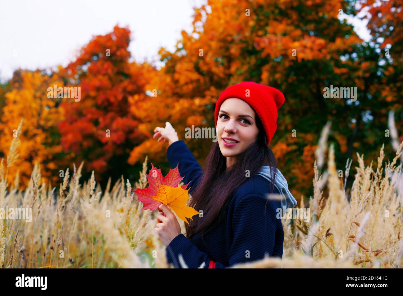 Femme souriante dans un chapeau rouge pointant vers la forêt d'automne colorée derrière elle. Concept d'automne. Banque D'Images