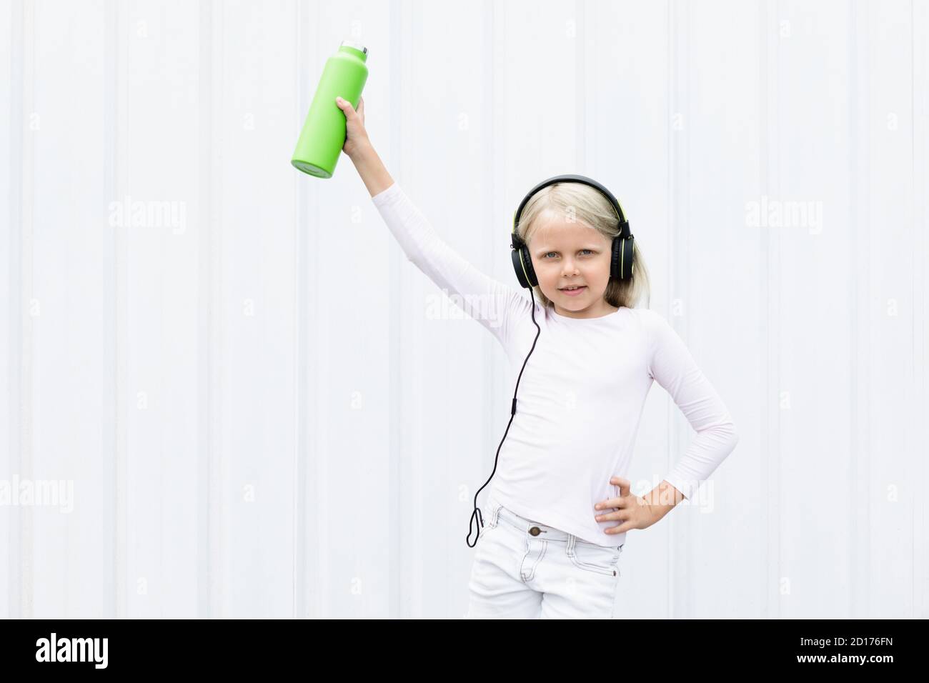 Jeune fille blonde sur fond blanc buvez de l'eau de source fraîche provenant d'un flacon vert réutilisable. Un style de vie sain en ville d'été. Banque D'Images