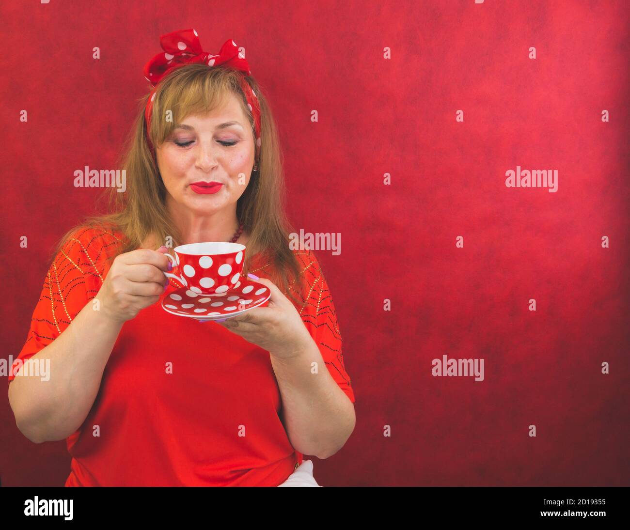 Femme en rouge posant sur fond rouge. tasse à pois avec soucoupe dans les mains. Style amusant Banque D'Images