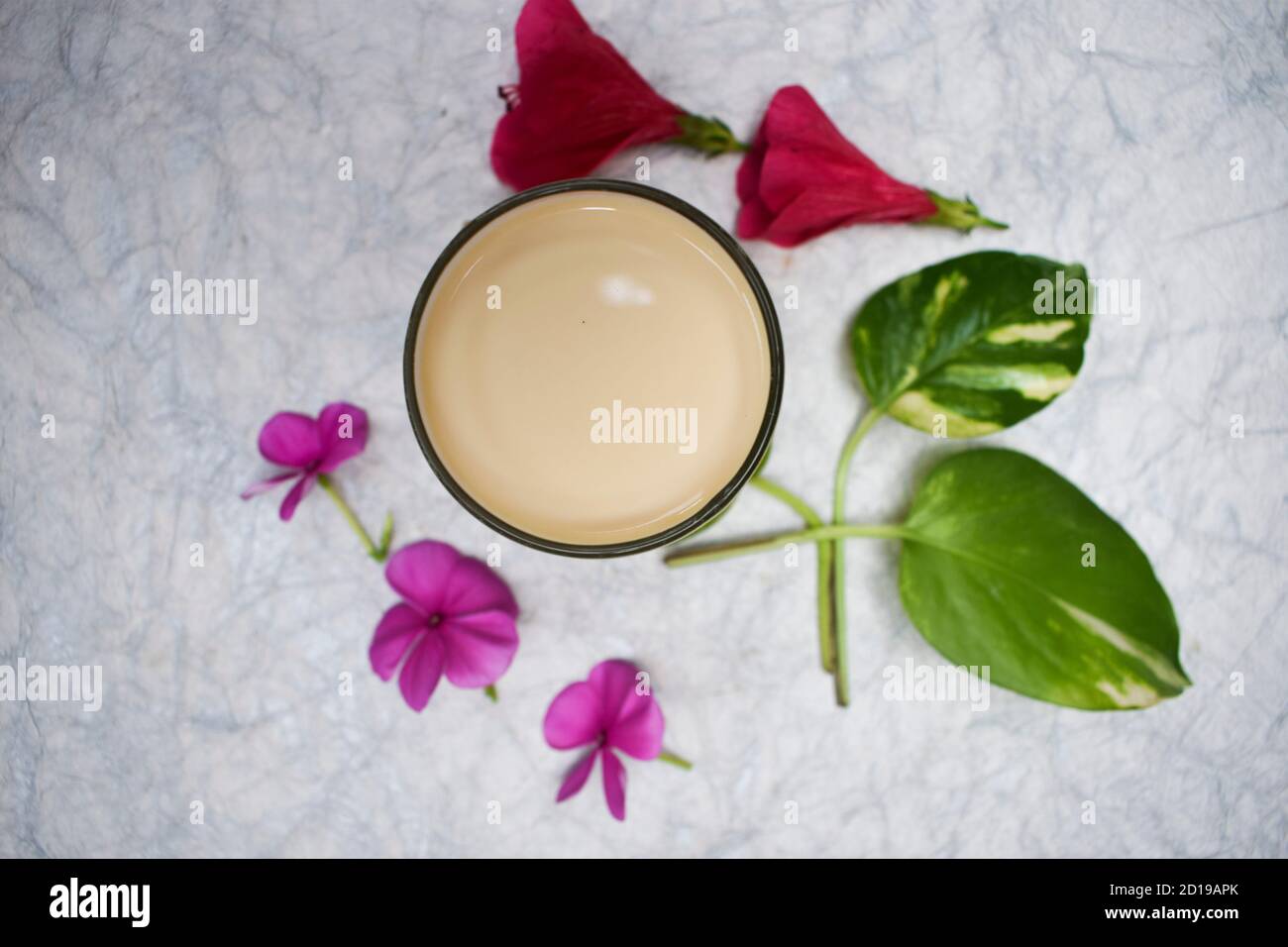 Vue de dessus du milk shake de Badam, lait traditionnel d'amande indienne en verre transparent décoré de fleurs et de feuilles sur fond blanc Banque D'Images