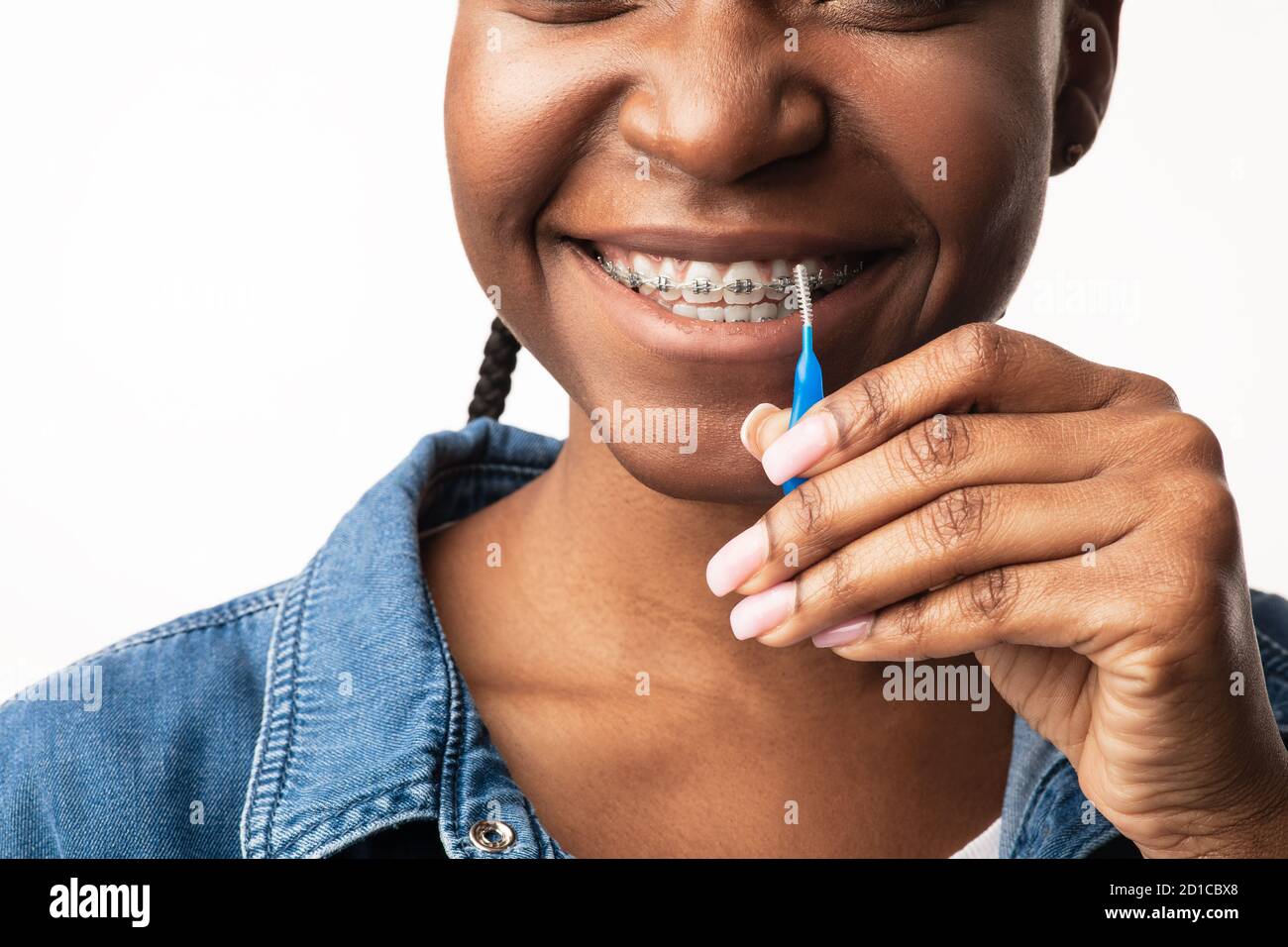 Femme noire nettoyage des dents avec des bretelles à l'aide d'une brosse, fond blanc Banque D'Images