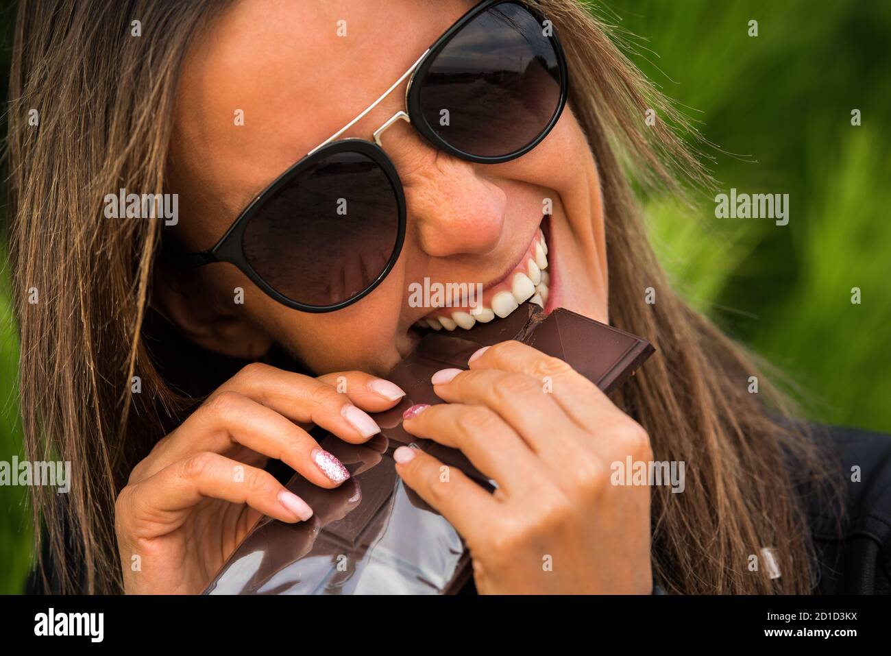 Jolie jeune femme fatiguée de stress et très heureuse de manger une barre de chocolat noir. Mordre le chocolat noir au coucher du soleil Banque D'Images