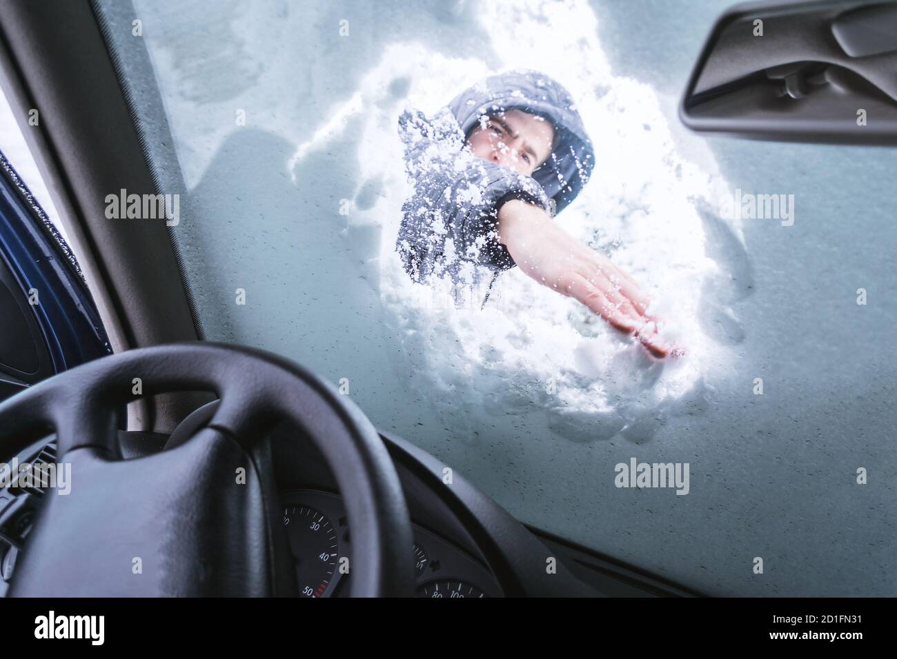 Homme en plein air nettoyant la neige sur le pare-brise de sa voiture. Vue de l'intérieur de la voiture. Banque D'Images