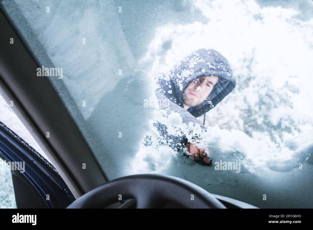 Homme en plein air nettoyant la neige sur le pare-brise de sa voiture. Vue de l'intérieur de la voiture. Banque D'Images