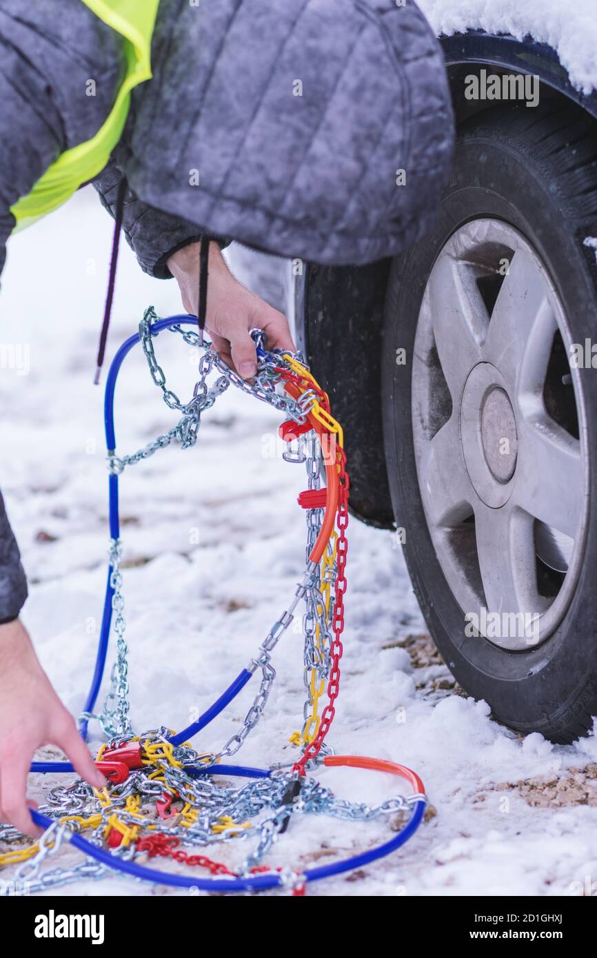 Homme préparant une voiture pour voyager le jour d'hiver. Chaînes à neige sur les roues de la voiture. Banque D'Images