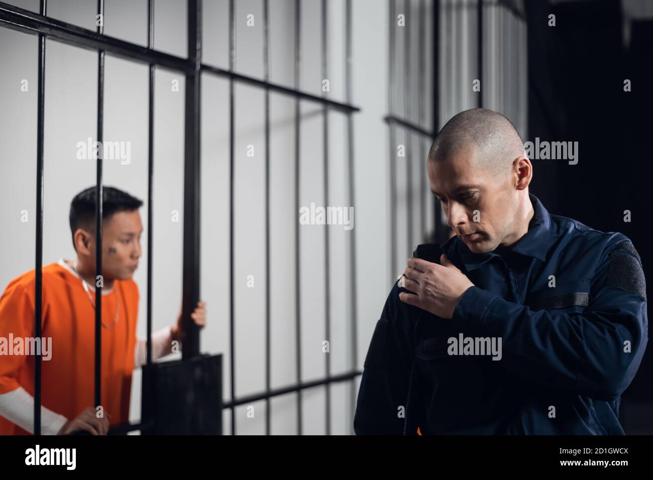 Un gardien de prison chauve et poupe fait les tours des cellules et transmet des informations par radio au chef du garde de prison Banque D'Images