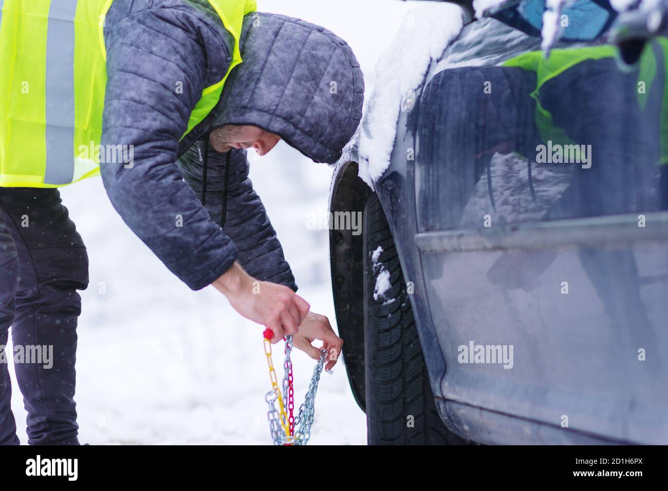 Homme préparant une voiture pour voyager le jour d'hiver. Chaînes à neige sur les roues de la voiture. Banque D'Images
