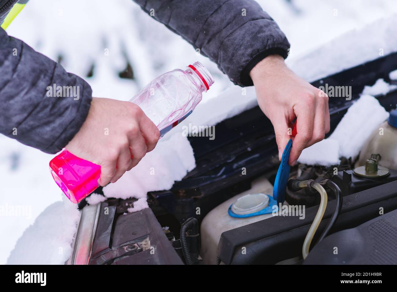 Vue rapprochée des mains avec le flacon versant du liquide de refroidissement antigel dans le moteur de la voiture par temps froid. Banque D'Images