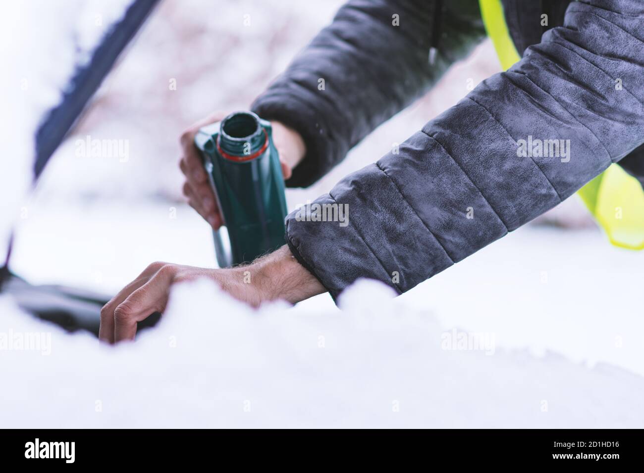 Vue rapprochée des mains avec une bouteille versant de l'huile moteur dans le moteur de la voiture par temps froid d'hiver. Banque D'Images