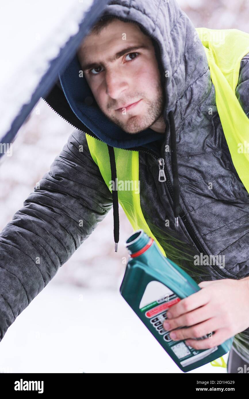Homme vêtu d'un gilet vert fluo versant de l'huile moteur sur le moteur de voiture à froid jour d'hiver. Banque D'Images