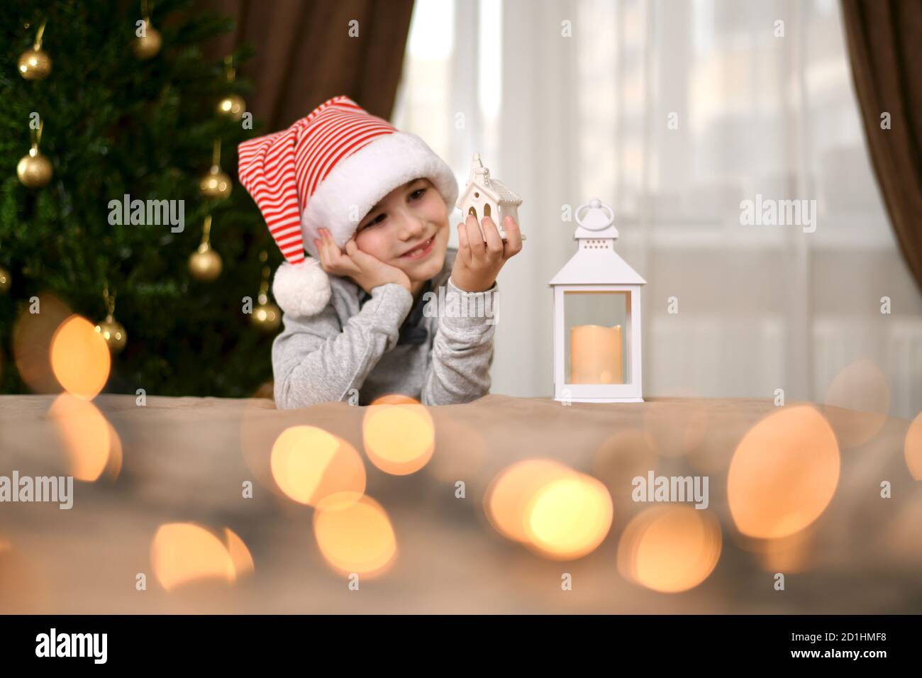 Une lanterne qui regarde une maison décorative, un jeune souriant, est assise avec un jouet dans sa main gauche et penchée sur sa paume droite. Banque D'Images