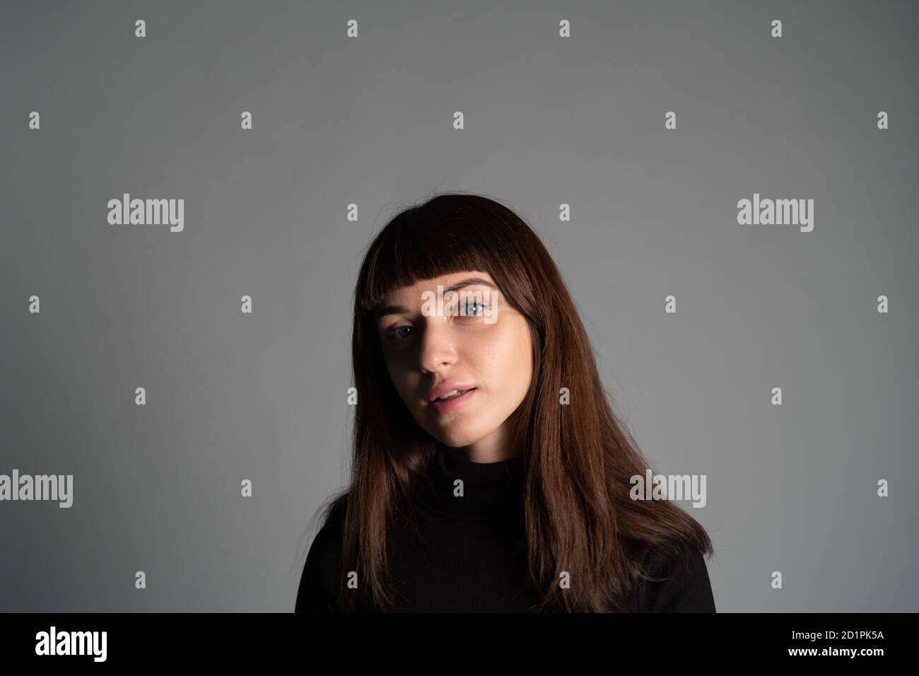 Gros plan portrait en studio d'une jolie femme brune, portant un pull à col roulé noir plié, regardant l'appareil photo, sur un fond gris Uni Banque D'Images