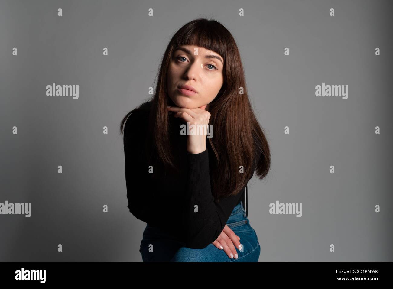Portrait studio d'une jolie femme brune, portant un pull à col roulé noir plié, regardant l'appareil photo, sur un fond gris Uni Banque D'Images