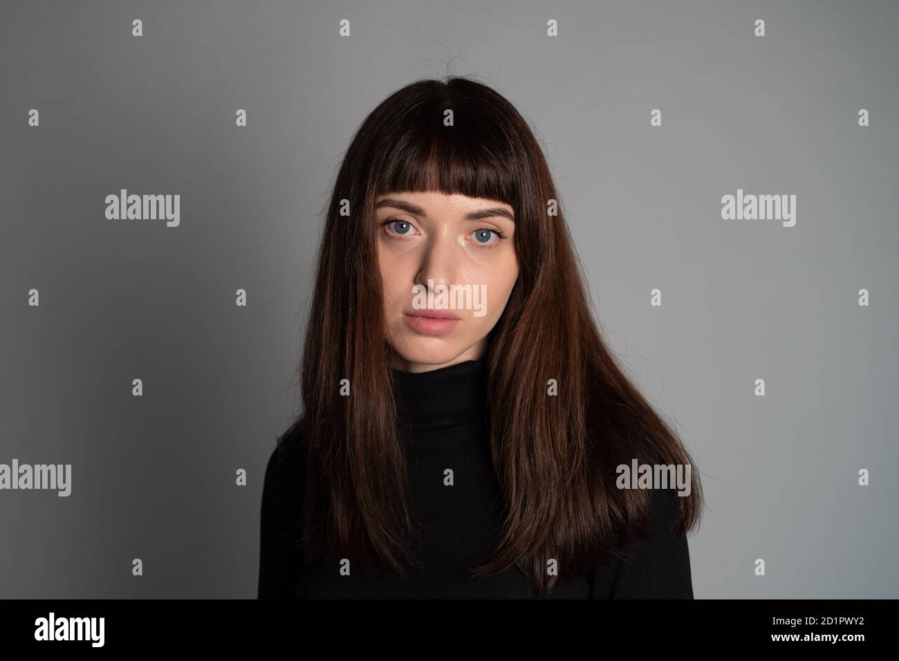 Gros plan portrait en studio d'une jolie femme brunette, regardant l'appareil photo, sur un fond gris Uni Banque D'Images