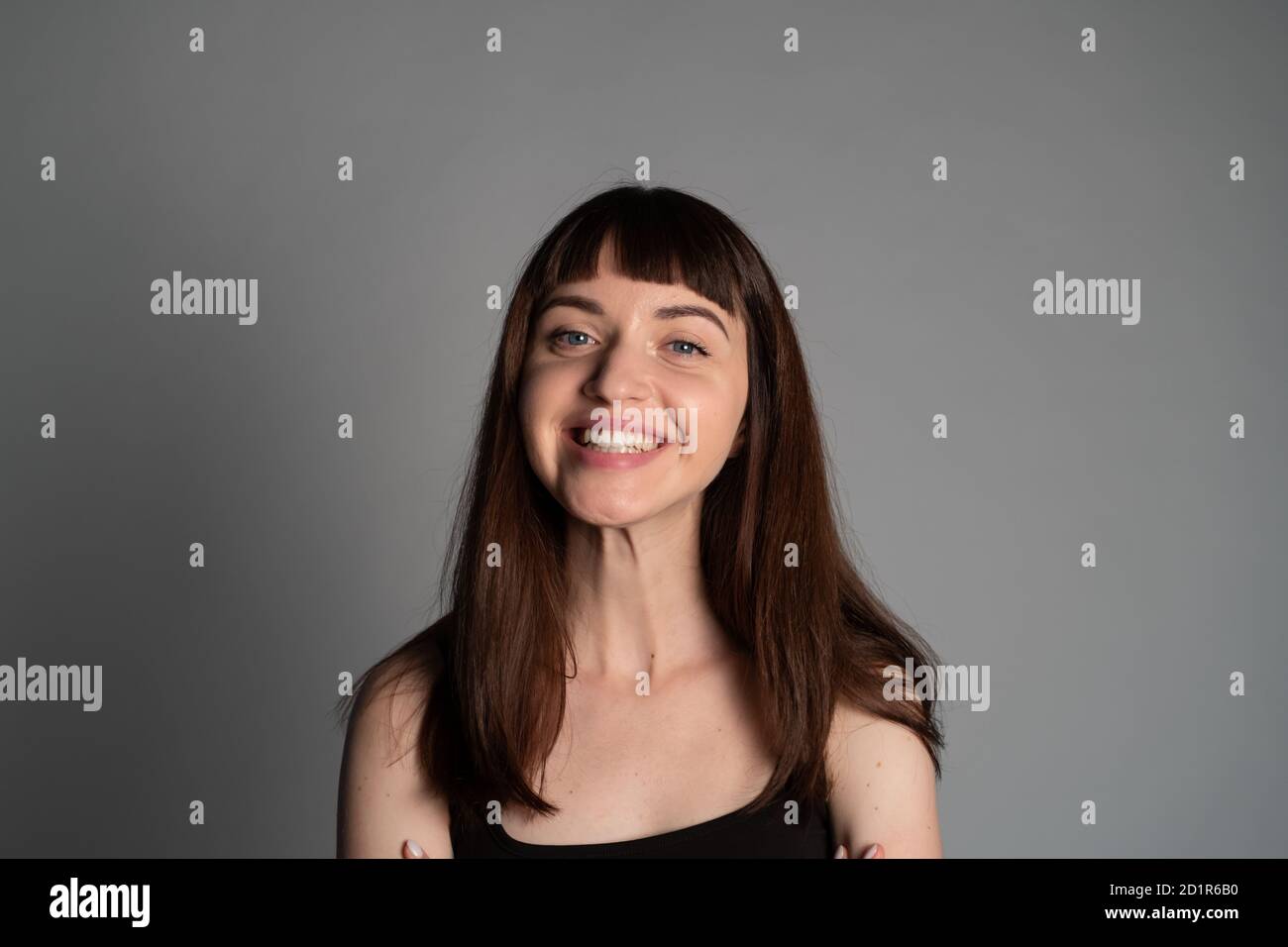 Portrait studio d'une femme souriante, portant un haut à bandoulière spaghetti, regardant l'appareil photo, sur un fond gris Uni Banque D'Images