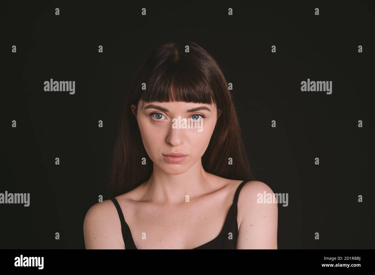 Portrait studio d'une jolie femme brunette dans un haut de bande spaghetti noir, regardant l'appareil photo, sur un fond noir Uni Banque D'Images