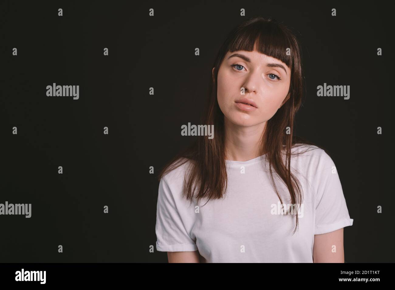 Portrait studio d'une jolie femme brune dans un t-shirt blanc, sur fond noir Uni, regardant l'appareil photo Banque D'Images