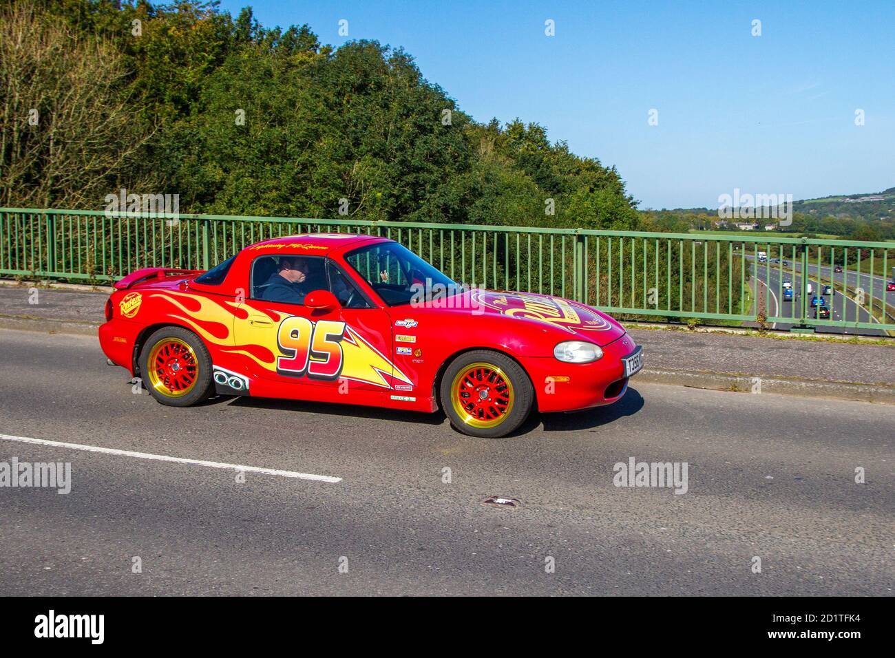 Roadster à essence rouge 1840cc 1999 90s années 90, autocollants de flamme rouge sur la voiture sportive Mazda MX-5 personnalisée en mouvement traversant le pont autoroutier près de Manchester, Royaume-Uni Banque D'Images