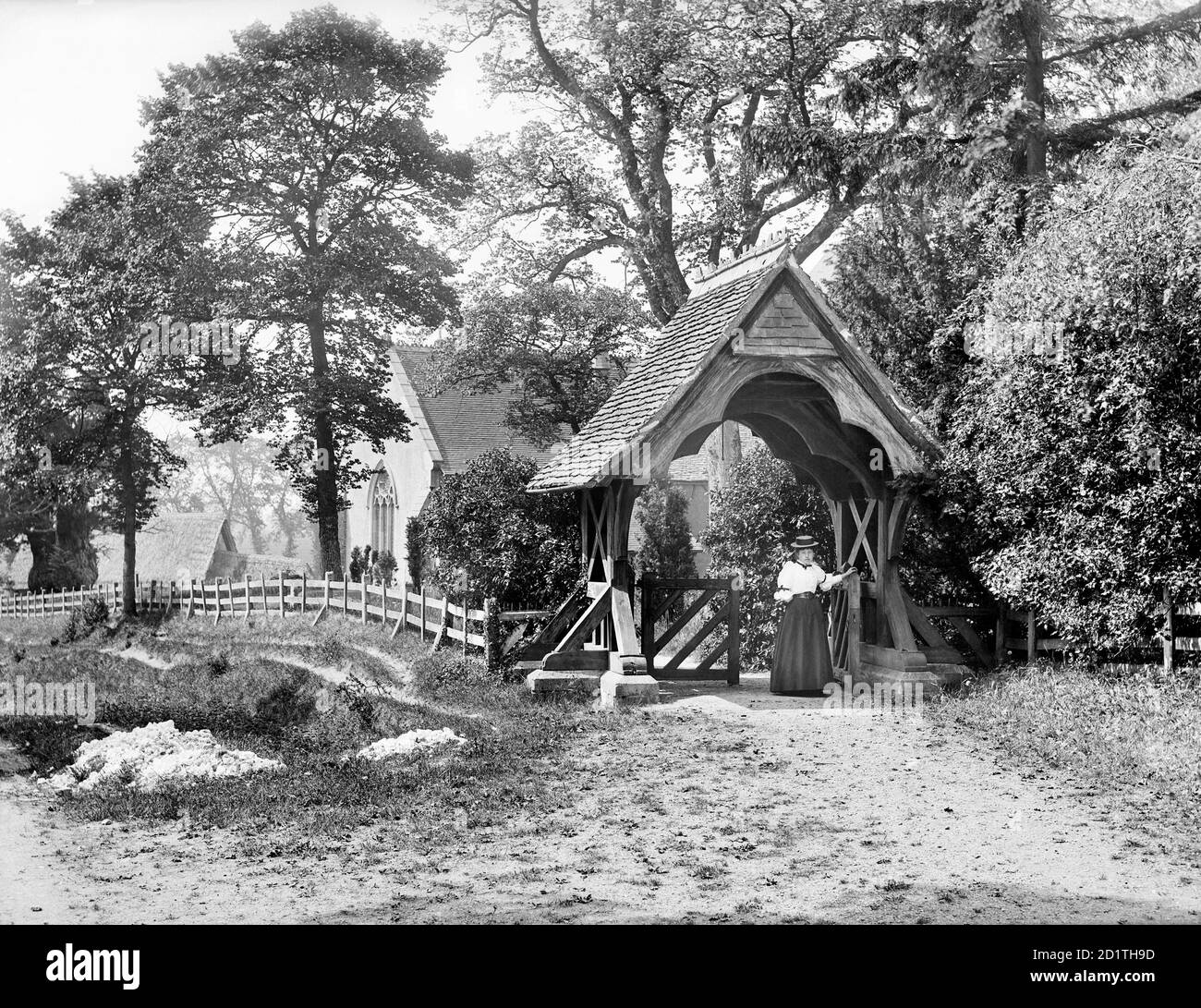 EGLISE ST MARYS, Aldworth, Berkshire. Regardant vers l'église qui est visible à travers les arbres avec une femme passant par le lychgate au premier plan. Photographié en 1895 par Henry Taunt. Banque D'Images