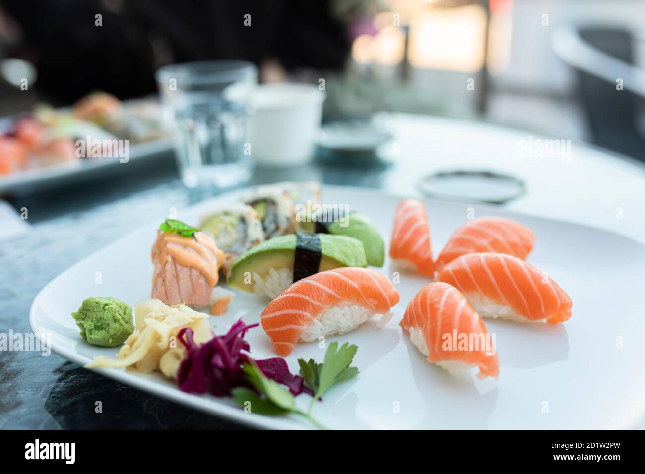 Une assiette de sushis sur une table à l'extérieur dans un restaurant. L'assiette contient des sushis nigiri au saumon, des sushis nigiri à l'avocat et des petits pains californiens. Une alimentation saine Banque D'Images