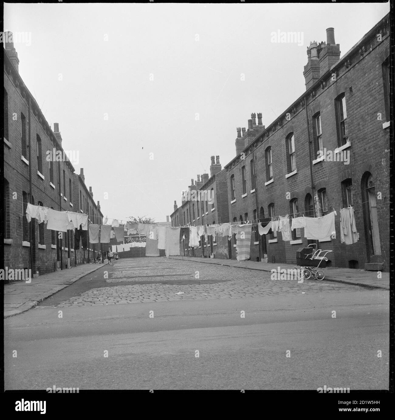 Lavage suspendu entre les maisons arrière-à-dos de Westlock Terrace ou de Westlock Crescent avec un emblème Burton visible ornant le mur au bout de la rue entourant Montague Burton Hudson Road Mills, Burmantofts, Leeds, Royaume-Uni. Banque D'Images