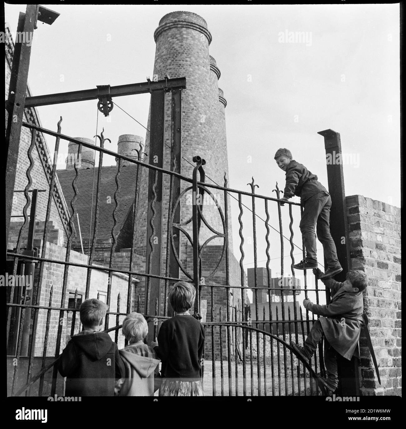 Un groupe d'enfants escaladant les portes en fer forgé à l'entrée latérale du canal vers George Goodwin et sas' Westwood Mills, Lichfield Street, Hanley, Stoke-on-Trent, Staffordshire, Royaume-Uni. Banque D'Images