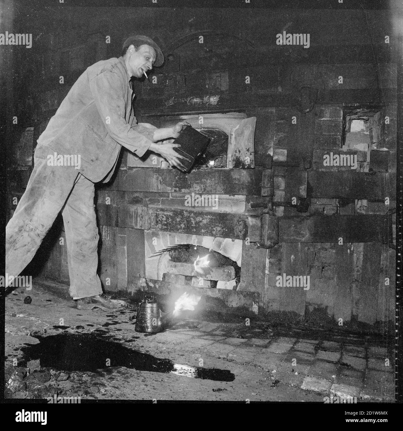 Un homme qui fait le feu sous un four dans une poterie non identifiée, Stoke-on-Trent, Staffordshire, Royaume-Uni. Banque D'Images
