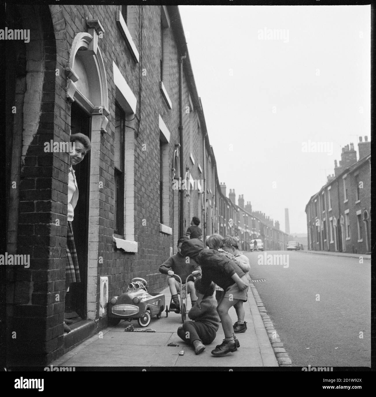 Enfants jouant sur le trottoir à l'extérieur d'une maison sur le côté nord de la rue Harper (anciennement la rue Albion) avec la cheminée de la poterie Stanley sur Newport Lane en arrière-plan. Banque D'Images