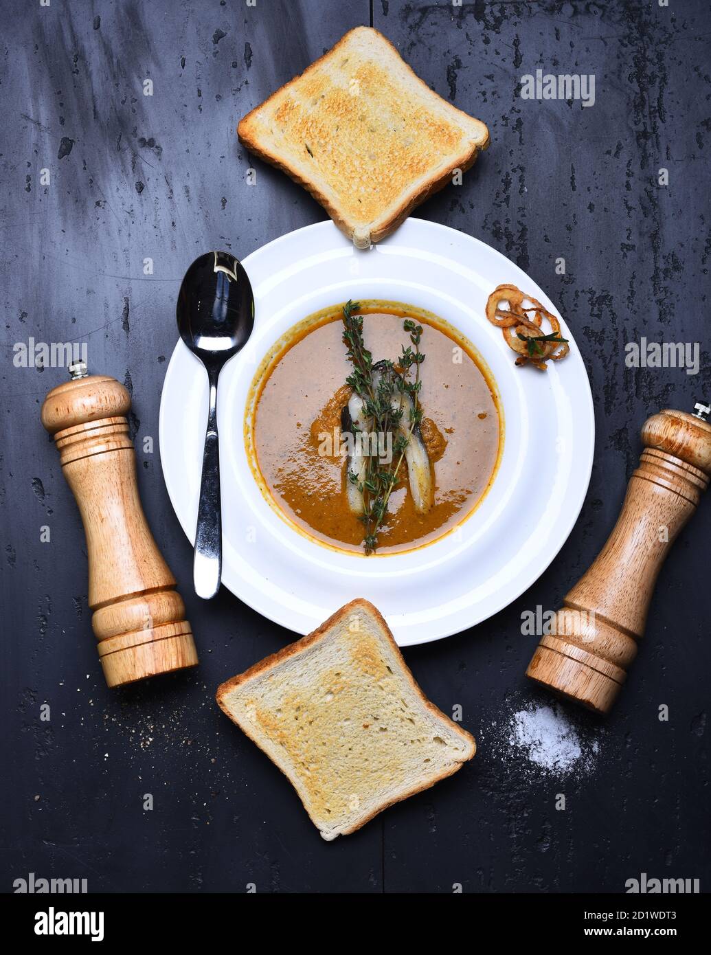 Concept de cuisine française. Soupe à la crème ou purée sur fond gris. Soupe de poisson avec un morceau de poisson et de thym et rondelles d'oignon sur une assiette blanche. Griller les morceaux de pain, la boîte à poivre, la cave à sel et la cuillère sur le plat Banque D'Images
