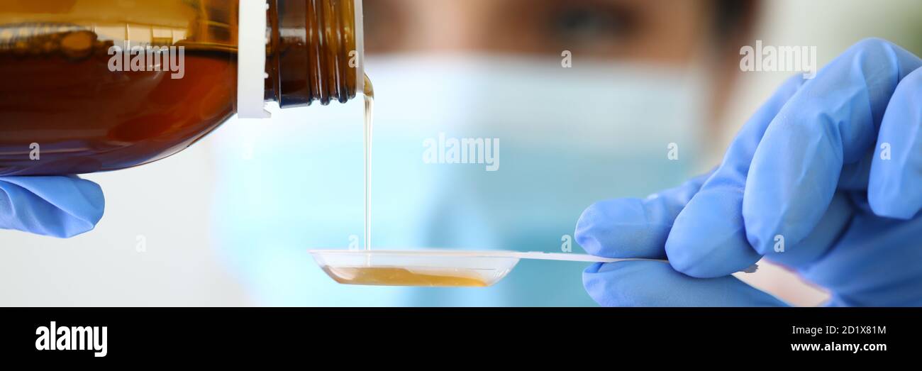 L'infirmière verse du sirop froid médicamenteux dans une cuillère en plastique. Banque D'Images