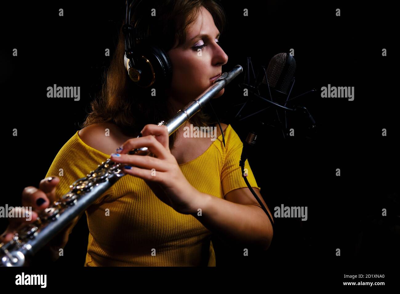La flûte à écouteurs joue dans le studio d'enregistrement. Enregistrez des instruments de musique à vent avec un microphone professionnel. Femme flûtiste en jaune dre Banque D'Images