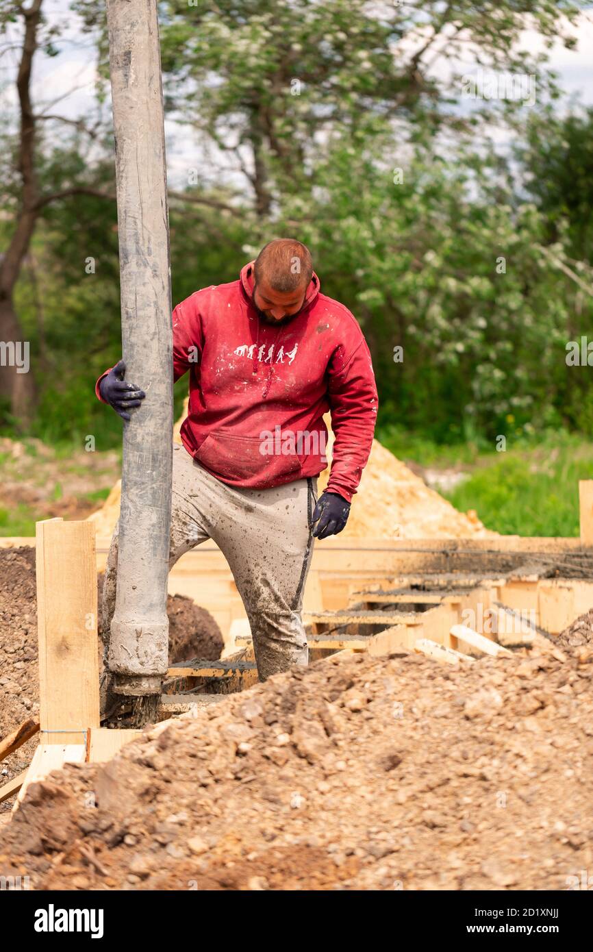 Ouvrier de construction posant du ciment ou du béton dans le coffrage de fondation avec pompe automatique. Fondation de la maison de construction Banque D'Images