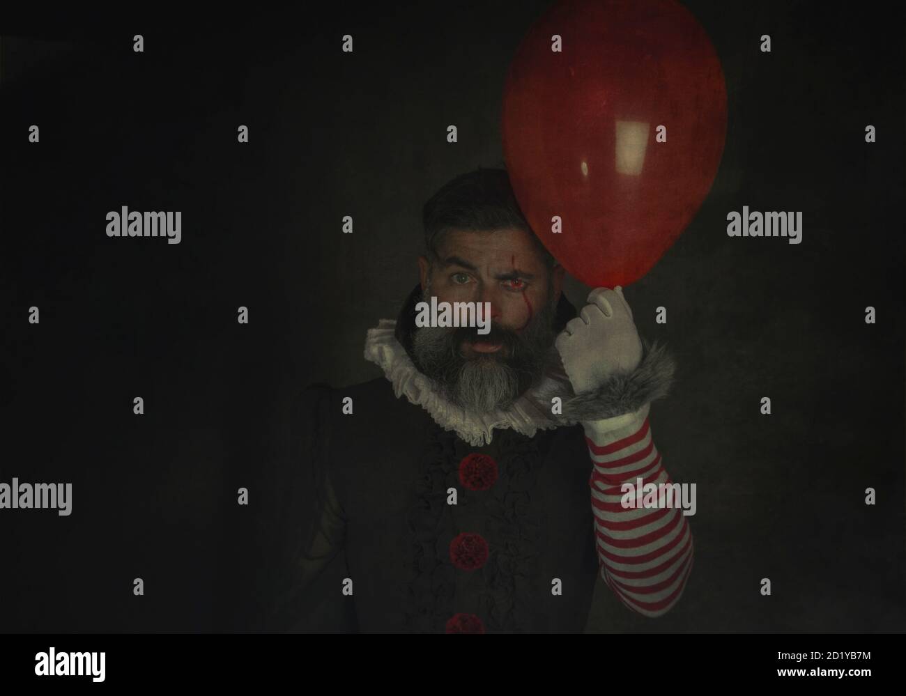 Mal et effrayant homme tenant le ballon rouge à la main sur fond noir .Halloween costume vintage. Peint Halloween maquillage de vacances. Banque D'Images