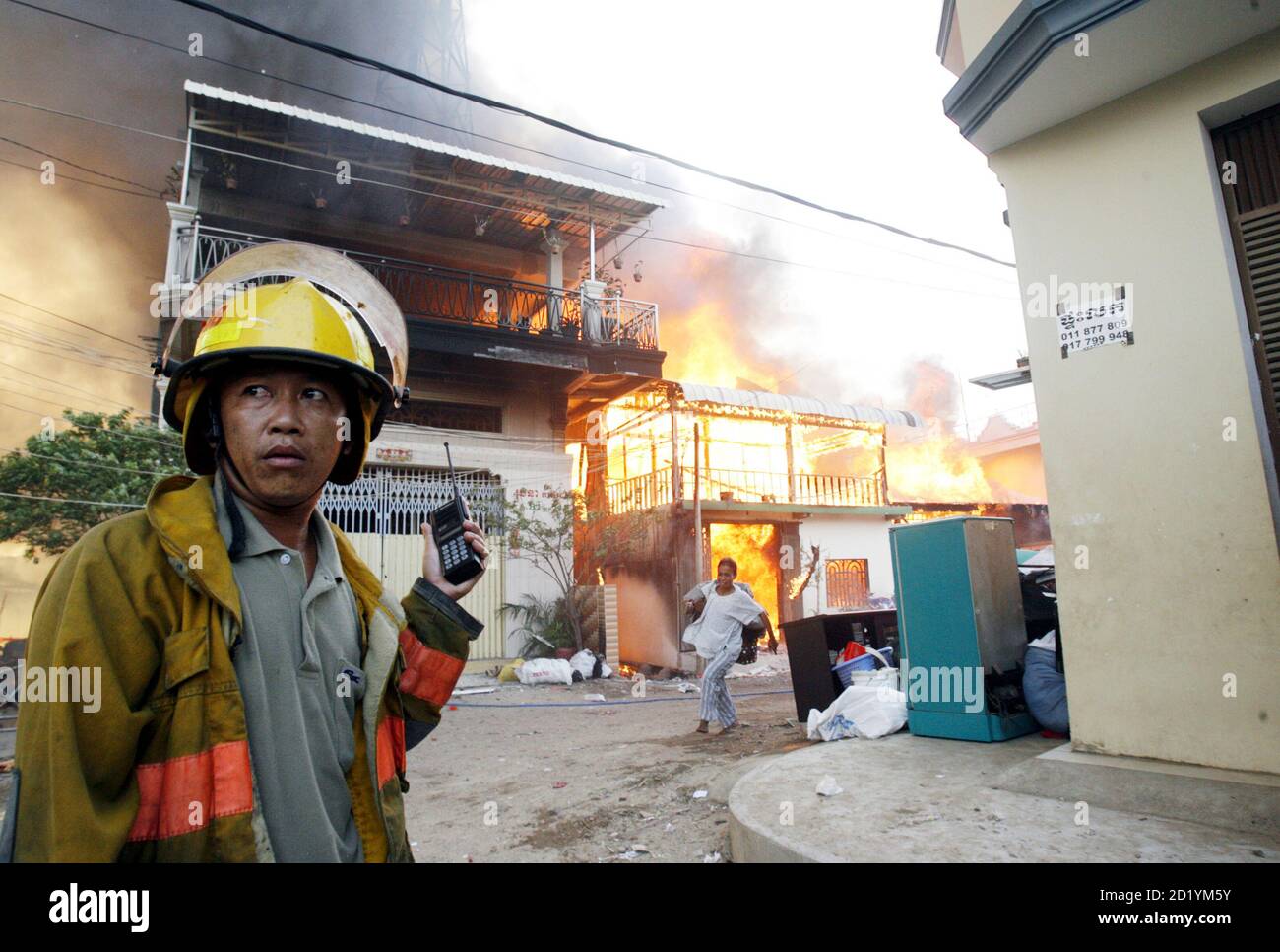 Un pompier écoute un poste de radio portatif comme une femme portant ses  effets fume sa maison brûlante à Phnom Penh le 11 avril 2008 . Au moins  plusieurs centaines de personnes