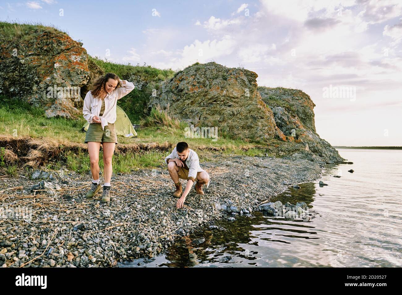 Jeunes couples de randonneurs choisissant des pierres sur le bord de l'eau tout en dépensant temps ensemble dans le pays Banque D'Images