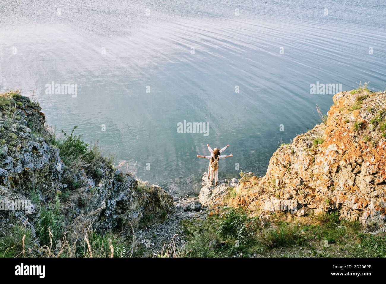 Au-dessus de la vue des voyageurs debout avec les bras étendus sur le rocher et en regardant la distance tout en profitant de la liberté au bord du lac Banque D'Images