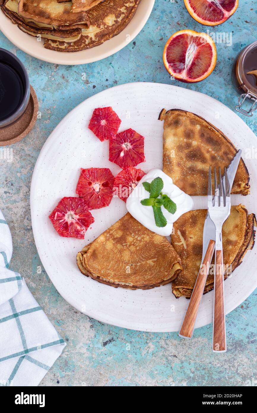 Crêpes fines avec sauce à la crème aigre, garniture au chocolat, menthe et pamplemousse sur une assiette bleue avec une serviette blanche Banque D'Images