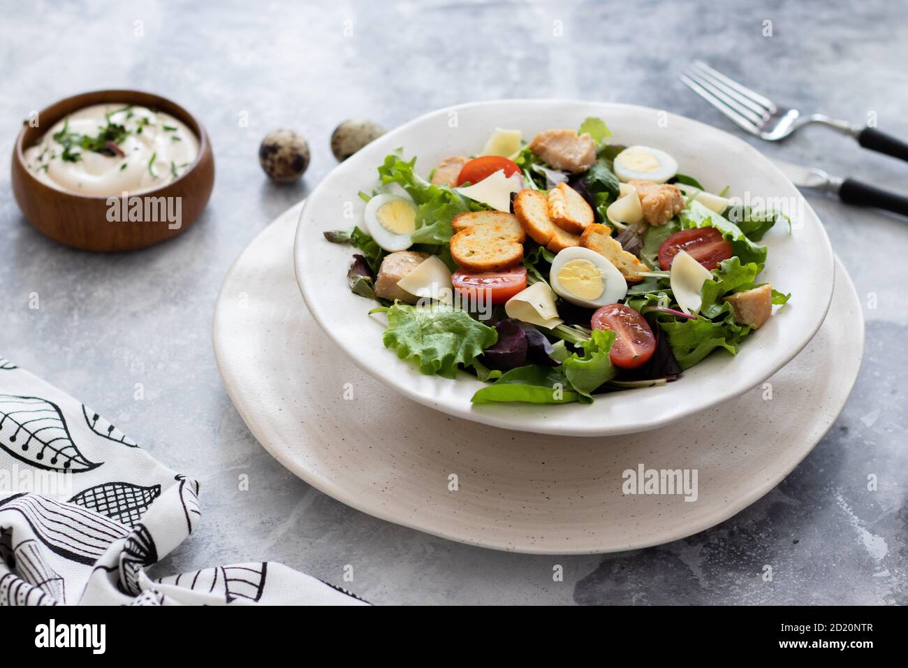 Salade César avec poitrine de poulet et œufs de caille avec césar sauce sur la table avec un bouquet de fleurs jaunes Banque D'Images